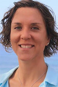 Smiling woman with short, curly hair against a blurred blue background.