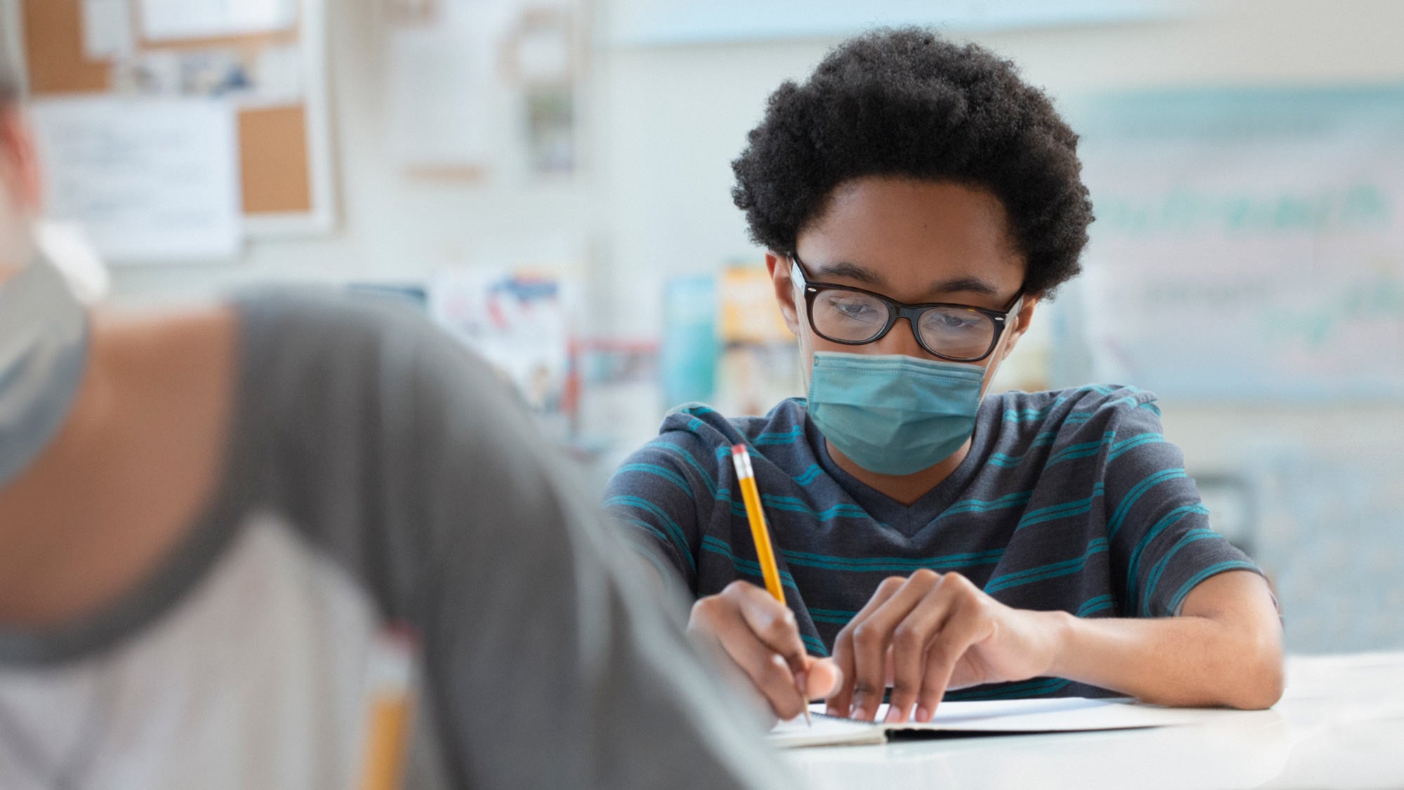 Masked boy, pencil in hand, at desk