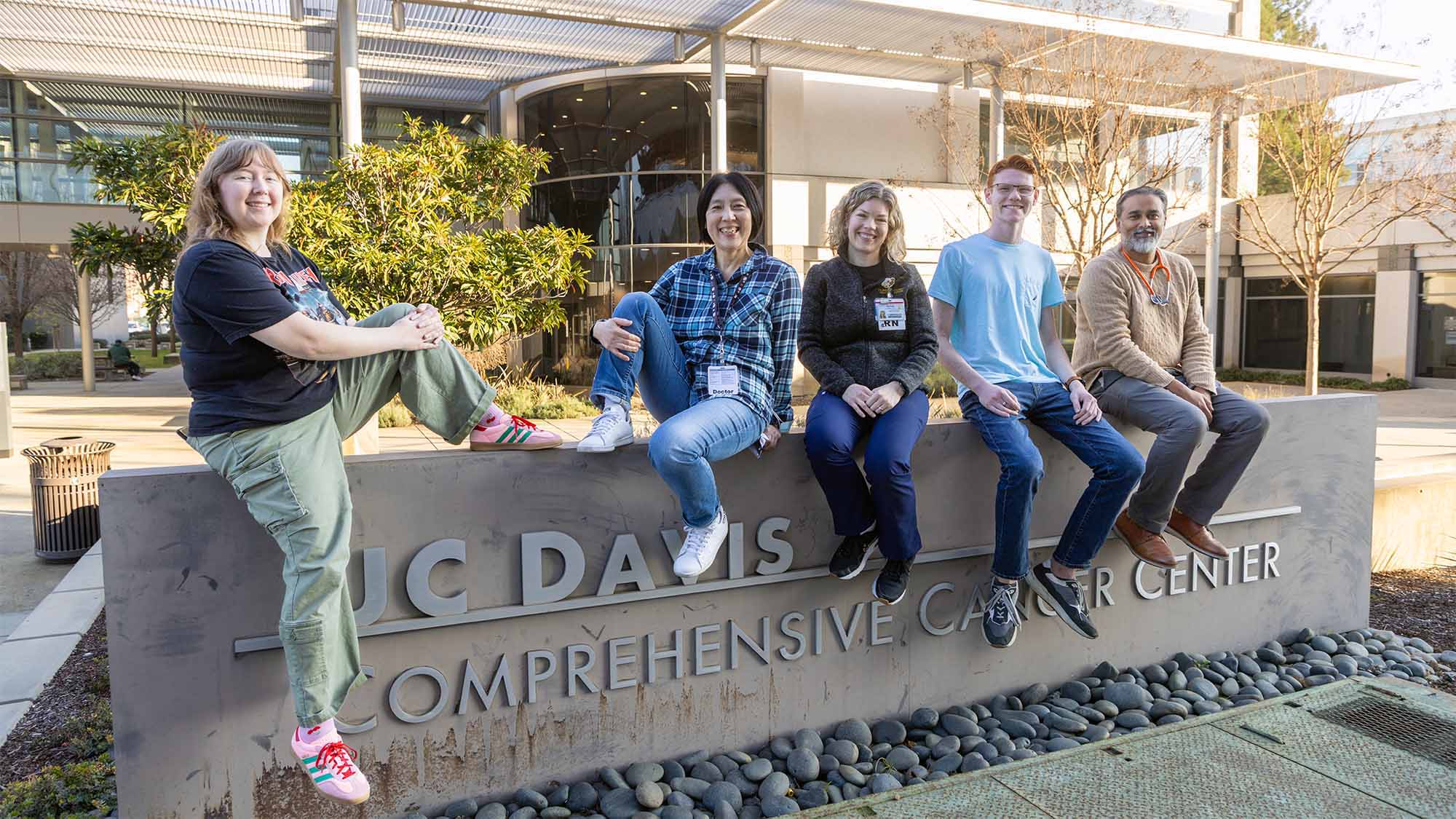 Five people pose casually on a stone sign for UC Davis Comprehensive Cancer Center.