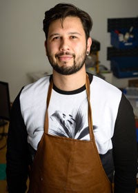 Photo of man with dark hair and beard in brown apron
