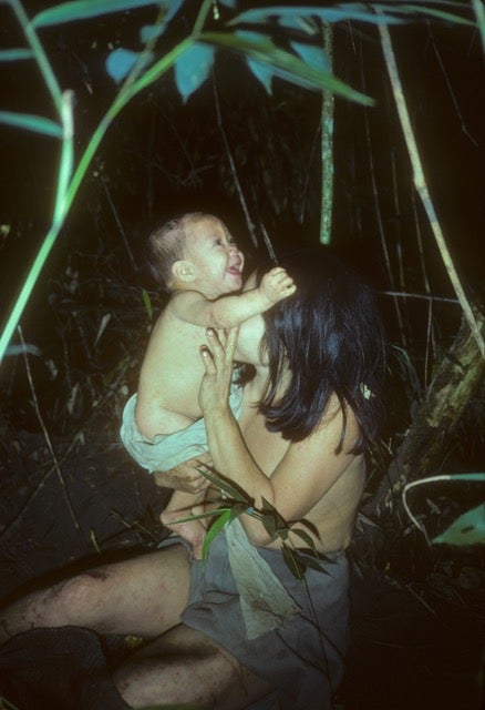 Photo taken at night shows a sitting woman, face turned away from the camera, holding a laughing baby. 