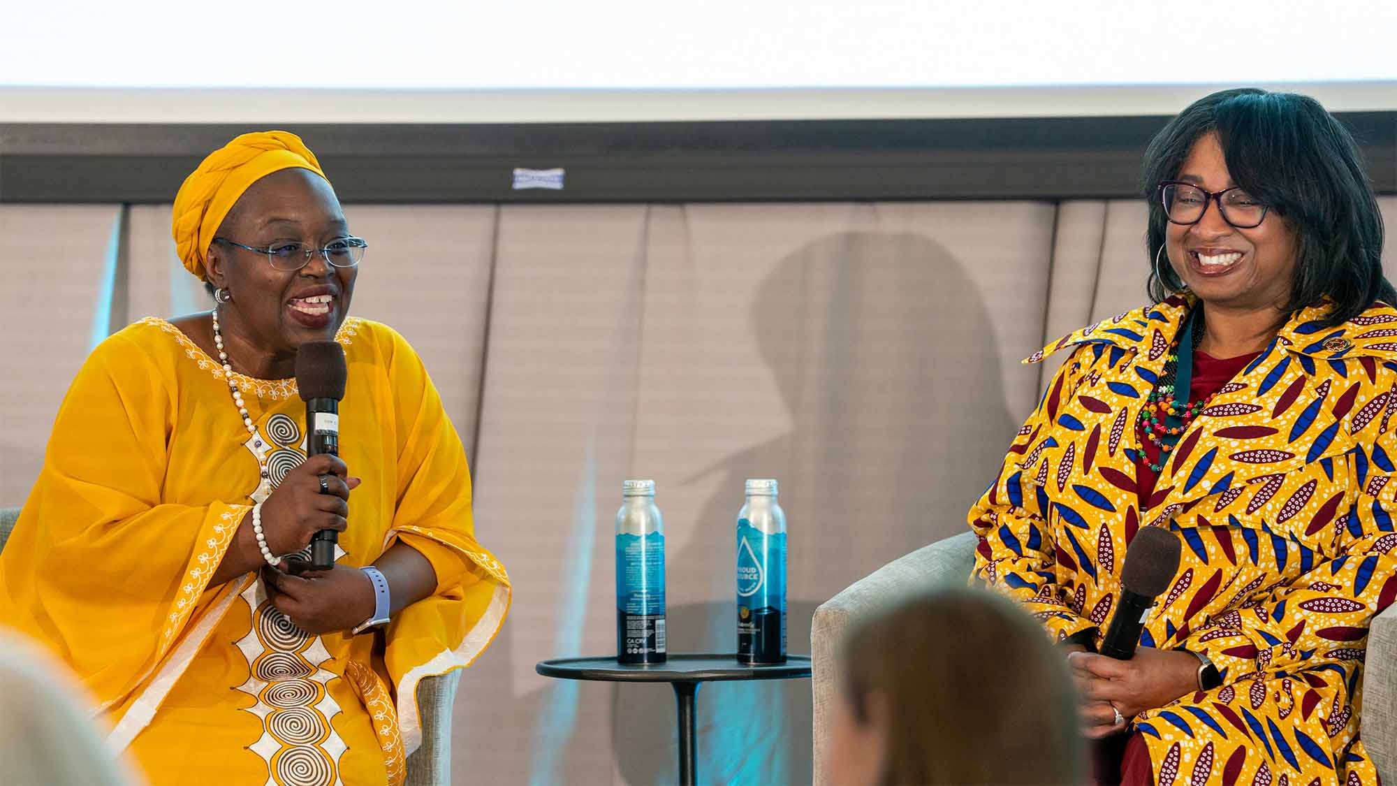Two people sit on stage and speak to crowd