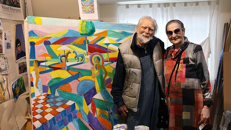Elderly couple smiling together in front of a colorful abstract painting.