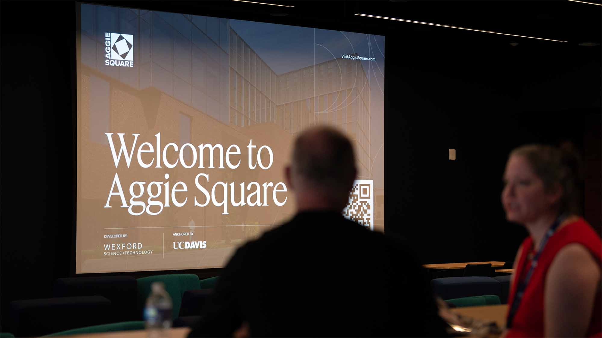 People talk in foreground. Sign in background says Welcome to Aggie Square