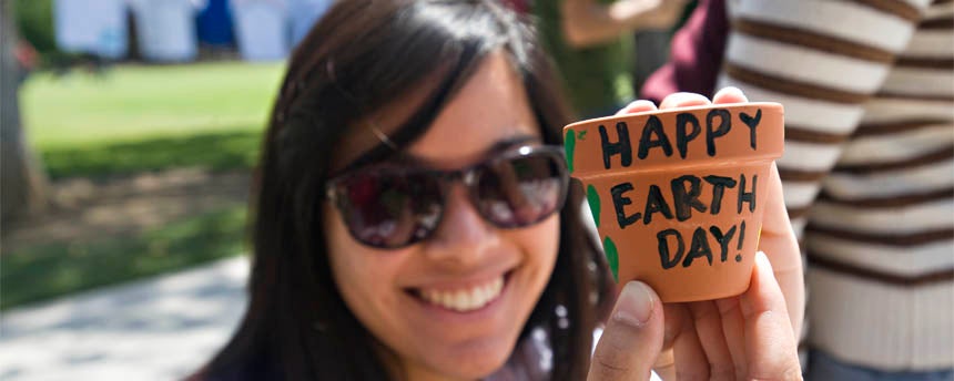A woman sitting outside shows her Earth Day painting to the camera