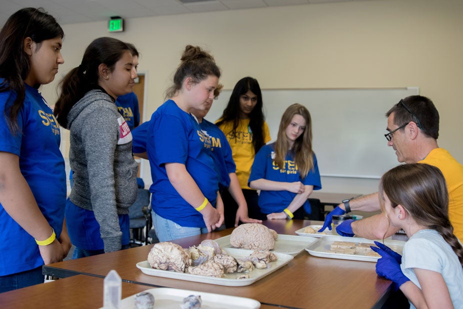 Girls gather around professor at a table.