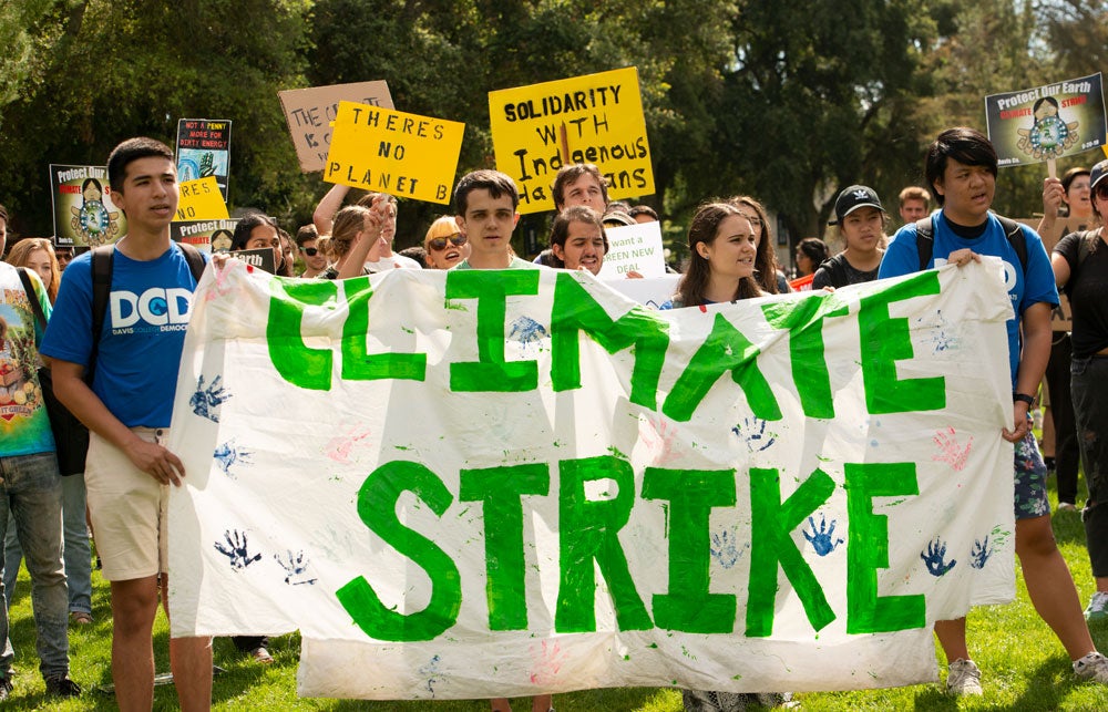 Climate strikers hold banner, "Climate Strike," green letters.