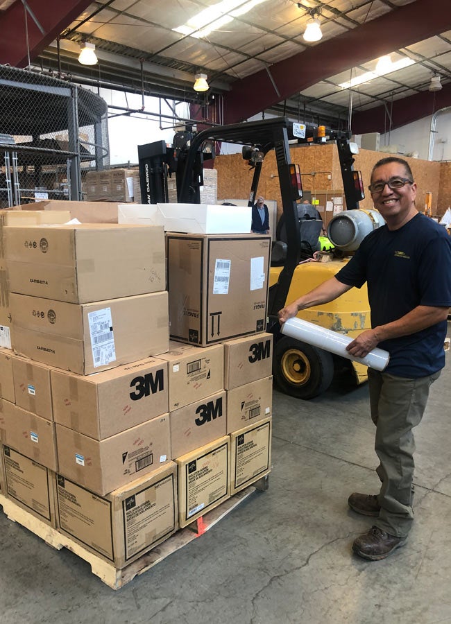 Man stands next to stack of supplies in warehouse.