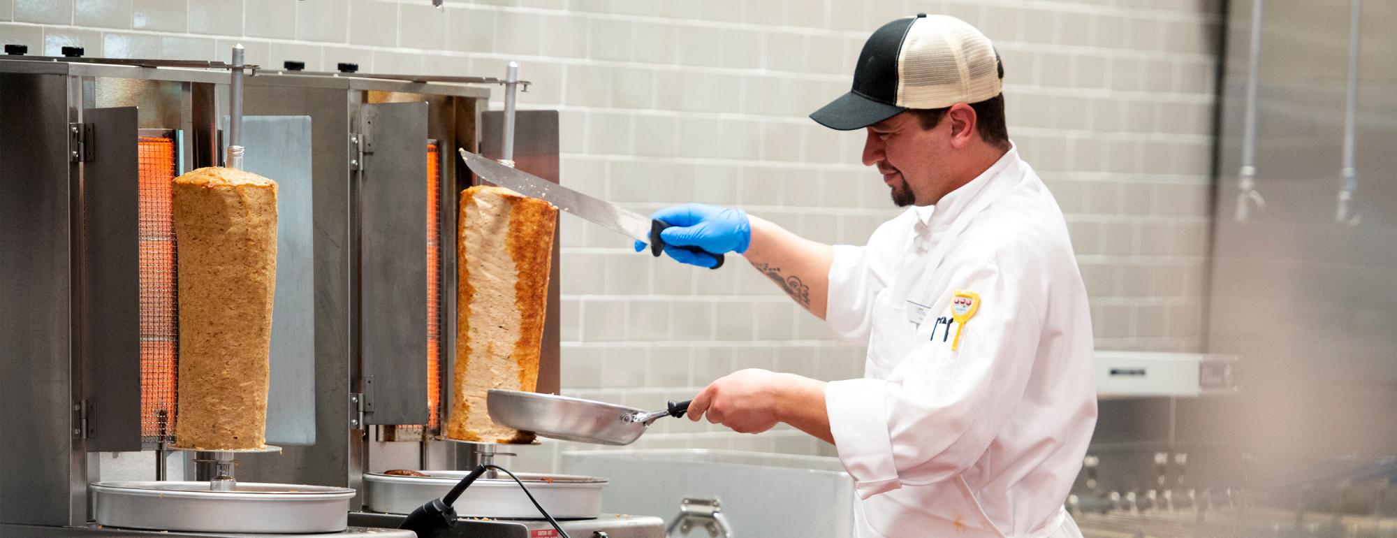 A chef slices meat from a large shawarma cone.