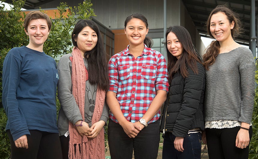 Five college women stand in garden in front of two-story orange building.