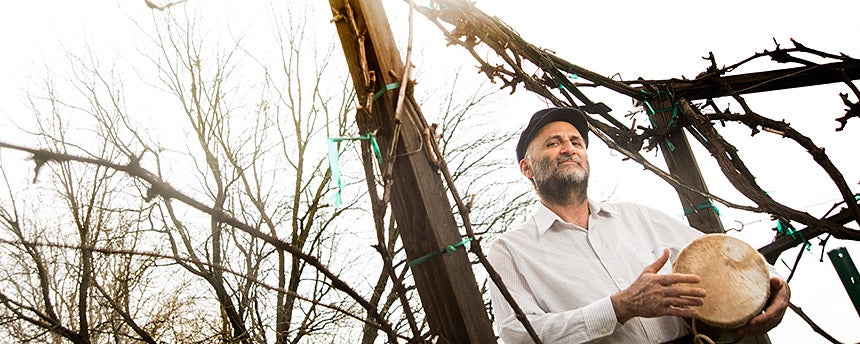 Man in beret under some bare vines holding a drum