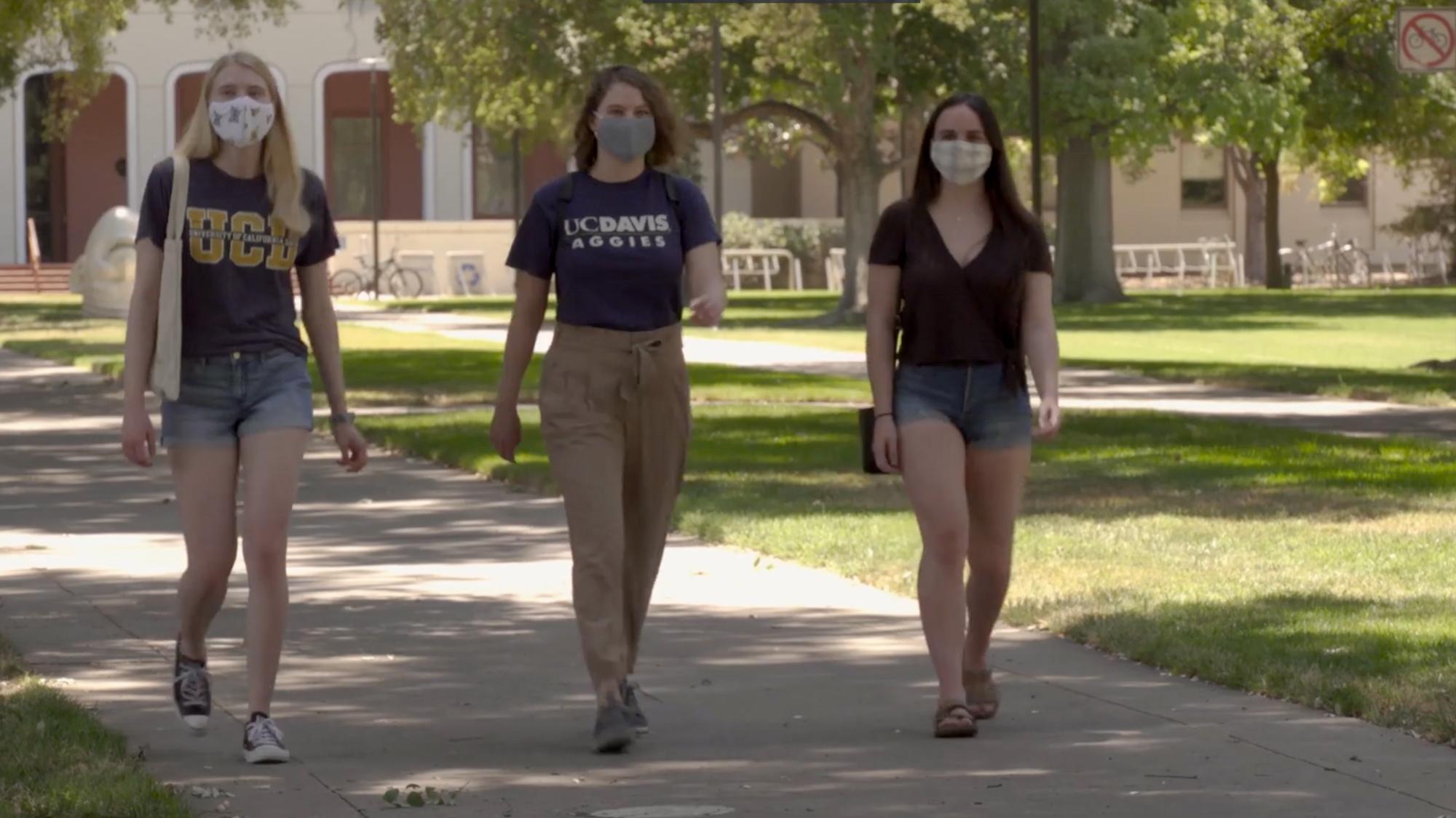 three students with masks walking on campus