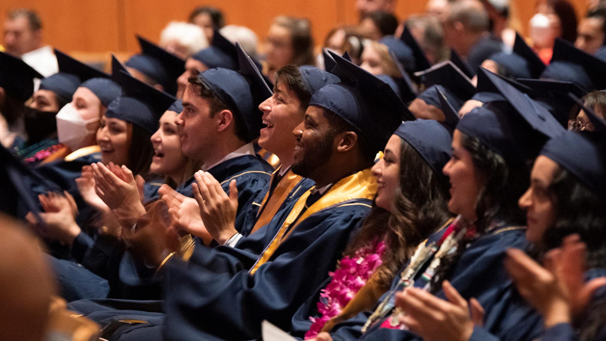 clapping and smiling students in caps and gowns in the Mondavi Center auditorium for a commencement ceremony
