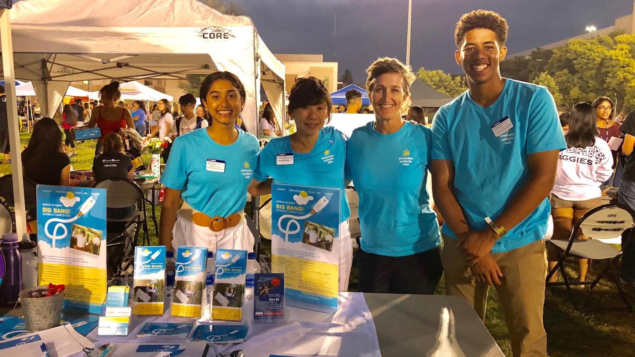Francesca D'Cruz with friends at an information booth outdoors. 