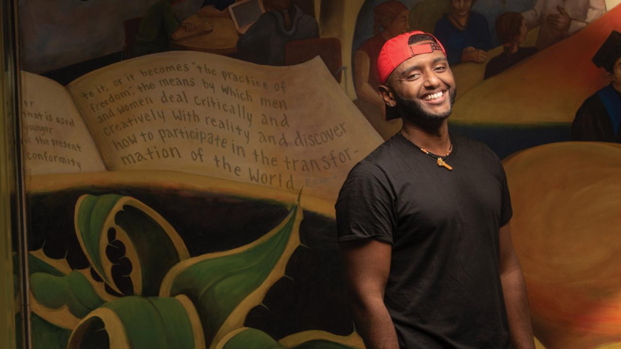 student posing for a photo in front of a wall with a painting