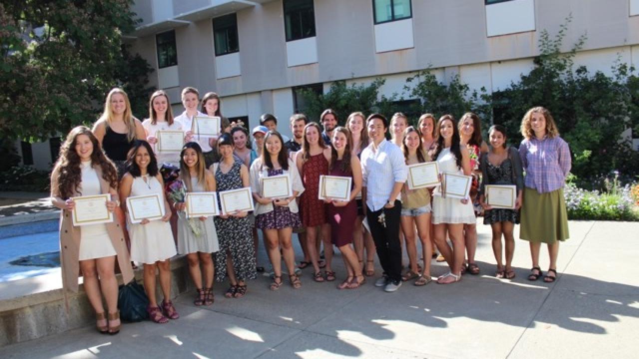 Students hold up their degrees in a cluster of 25 people. 