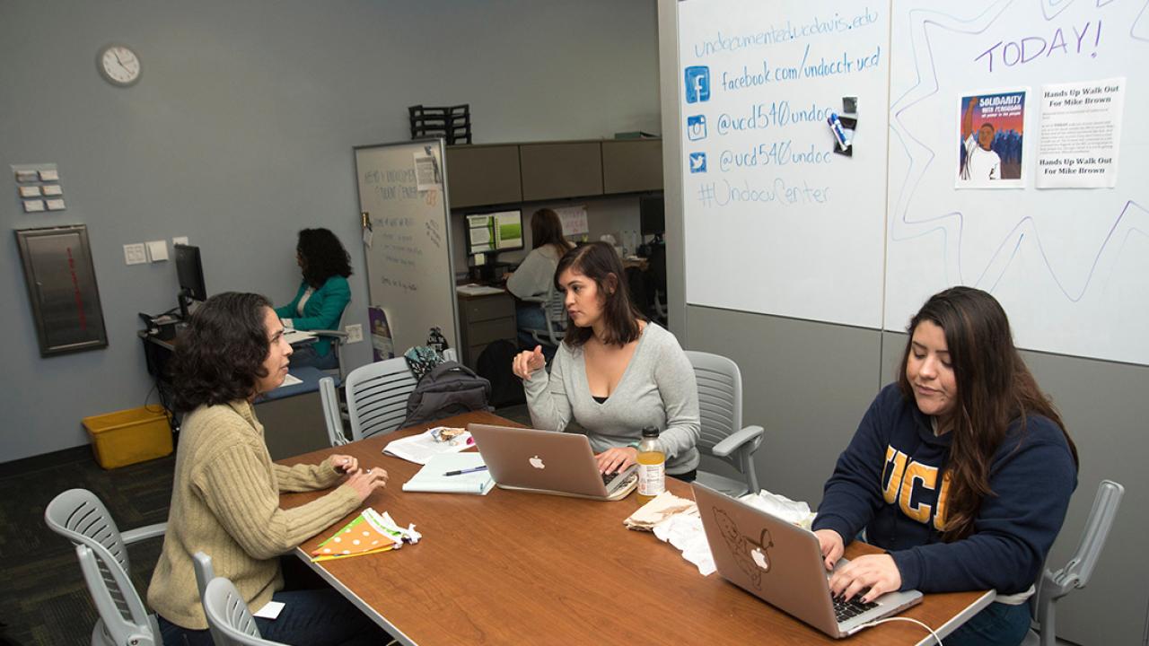 Three women sit around a table having a meeting.