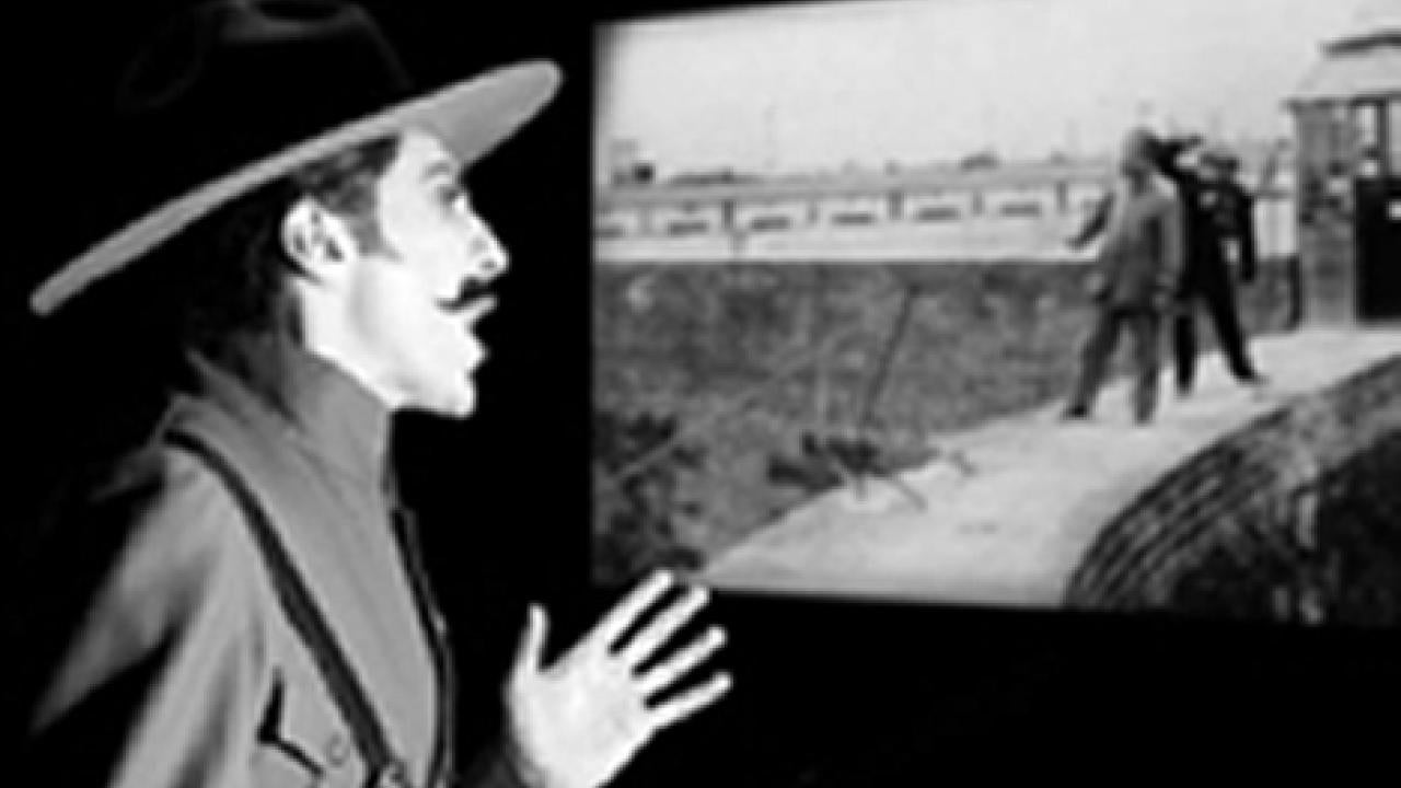 A narrator from the Japanese "benshi" tradition takes the stage in front of a screen on which a classic Mexican silent film is playing.