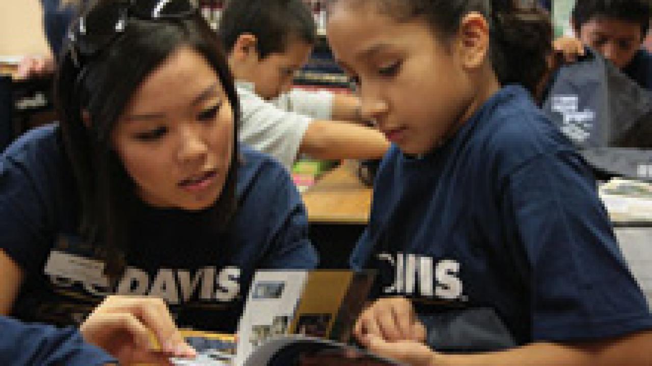 Alumna Julia Nguyen helps Oakland student Ana Melgoza through the Aggie Pride book. 