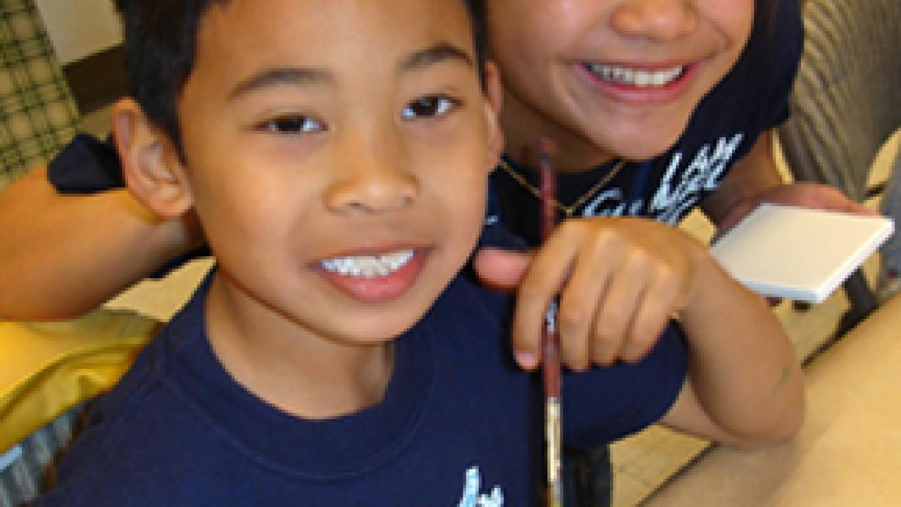 Julian Barker looks up from his artwork during a Campus Recreation activity, with staff member Nancy Nguyen looking over his shoulder.