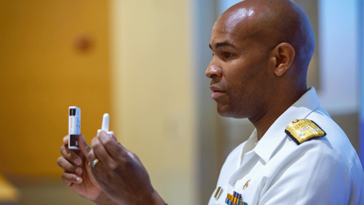 Physician in U.S. Public Health Service uniform, holds up two medications.niform