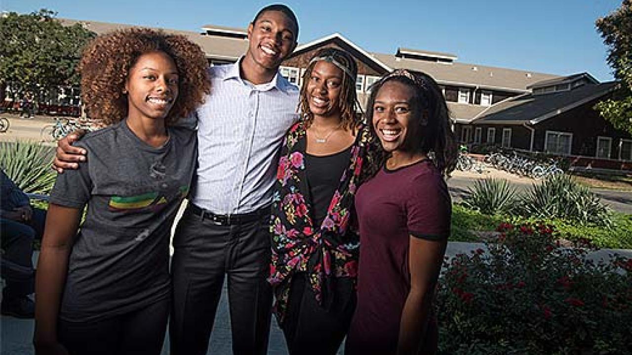 Four African American students standing in front of brown-shingled house