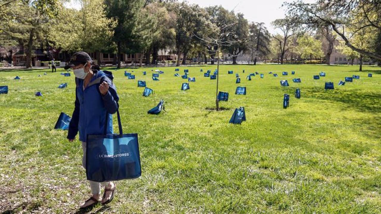 Two people take grocery bags, which are spaced wide apart on the Quad.