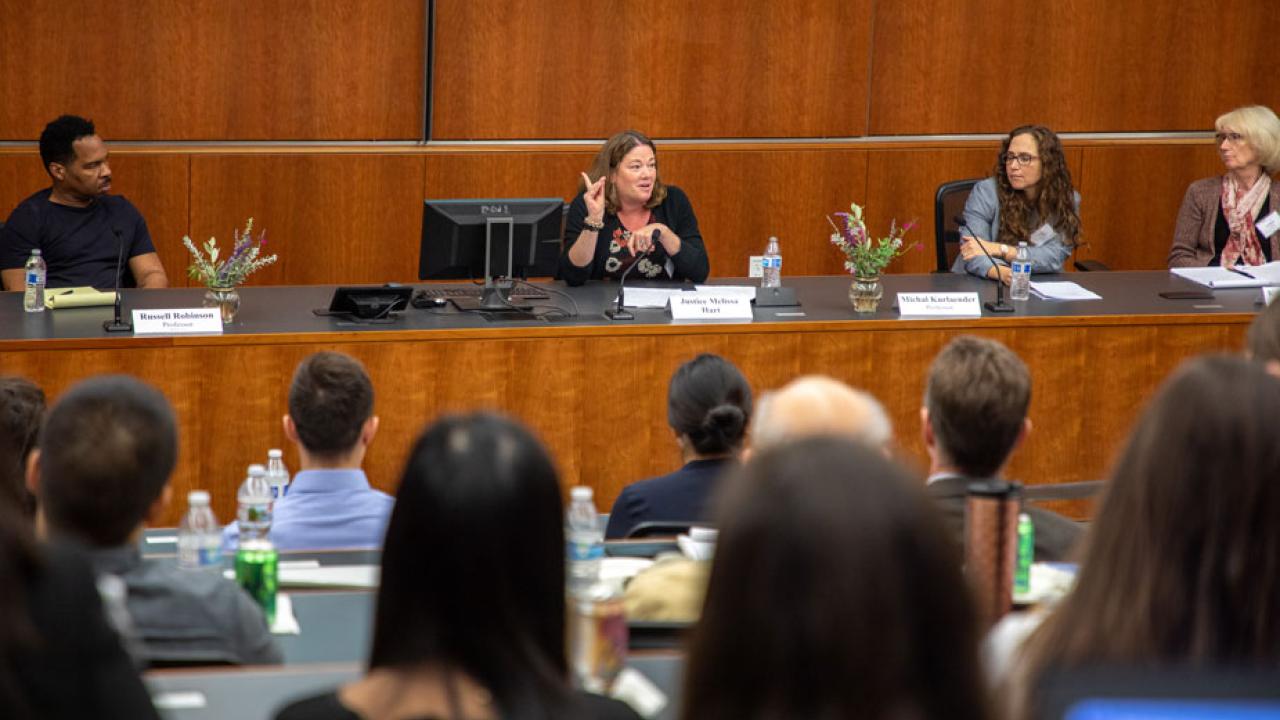 Woman gestures with pointed finger in the air, at center of dais.