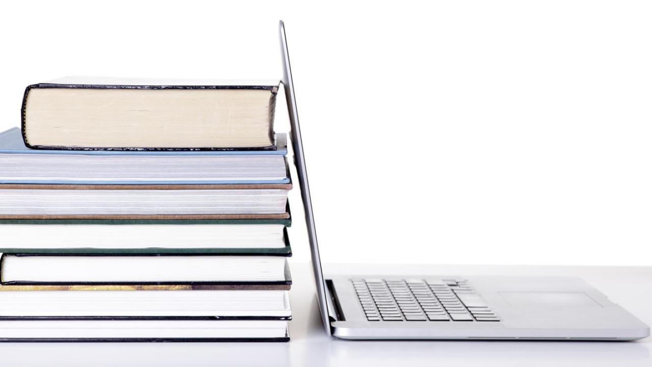 Stack of books next to an open laptop