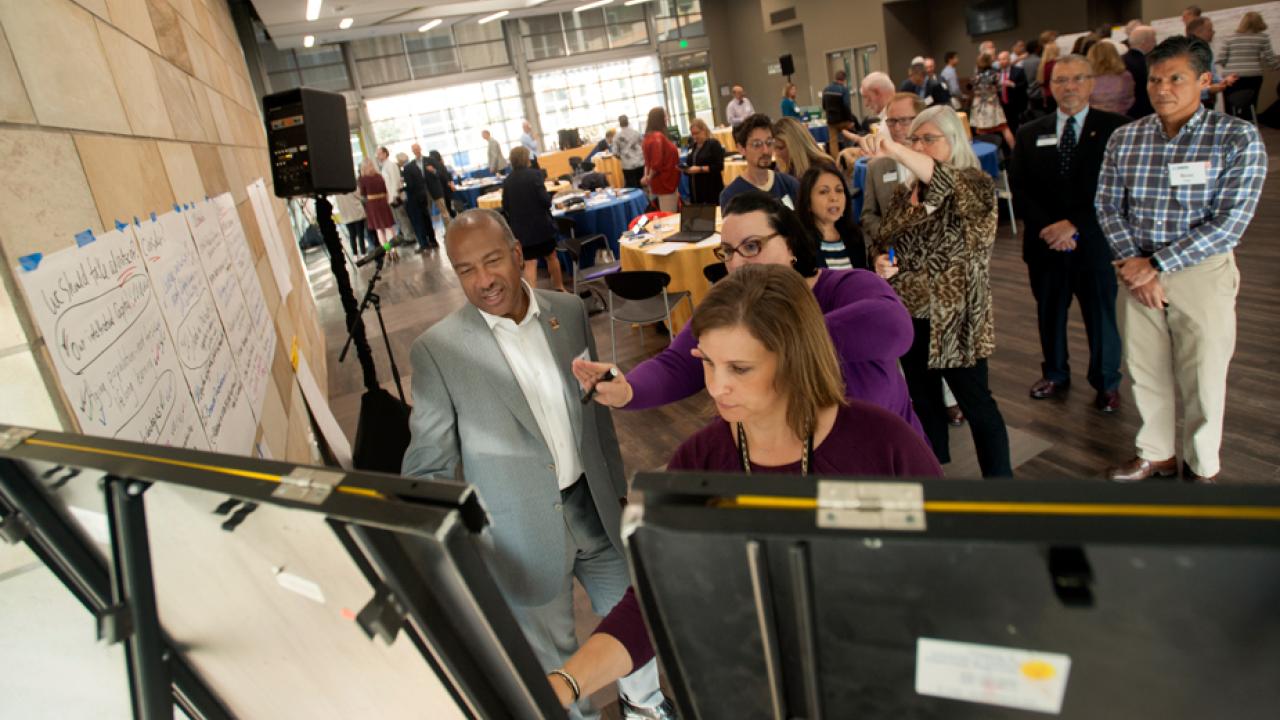 Chancellor and others writing on poster pads on easels.