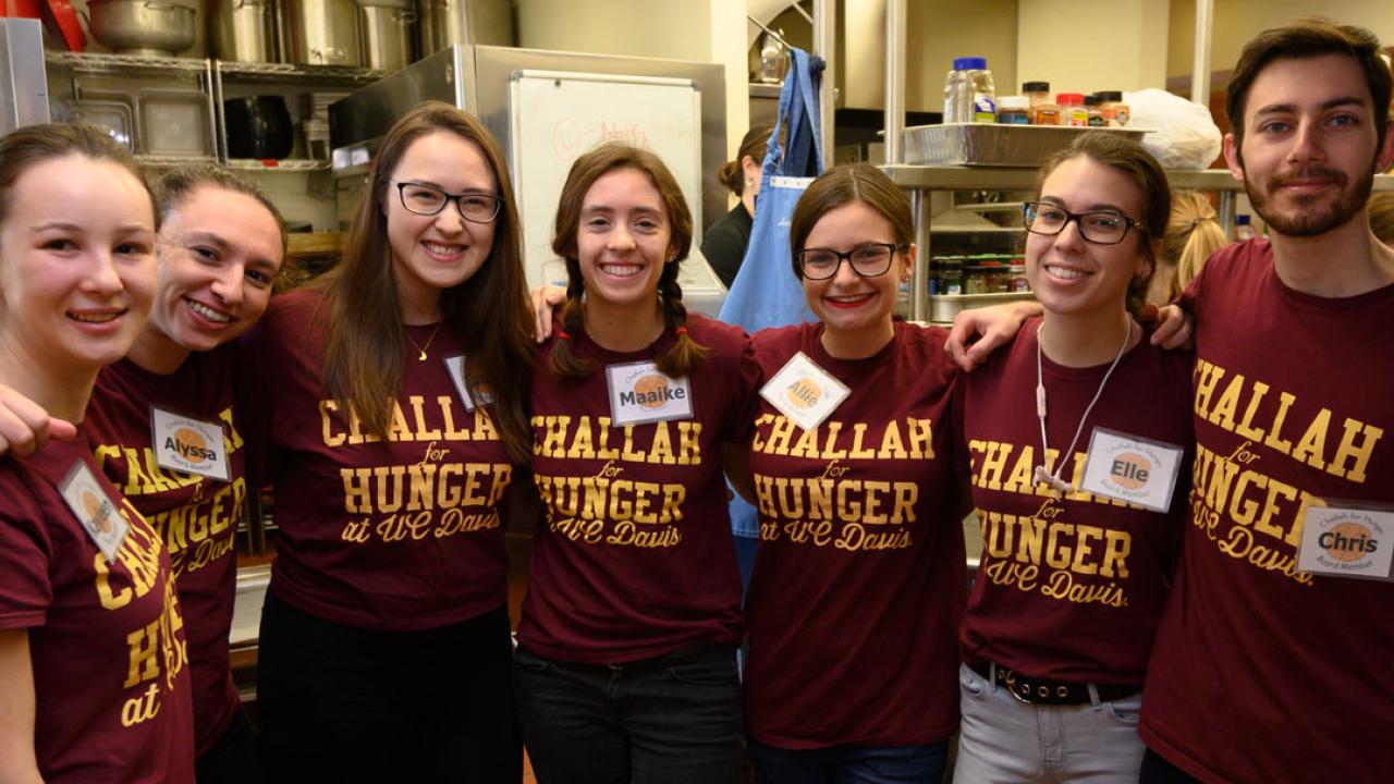 Students pose in a line in kitchen, all wearing burgundy T-shirts with &ldquo;Challah for Hunger UC Davis&rdquo; in gold.