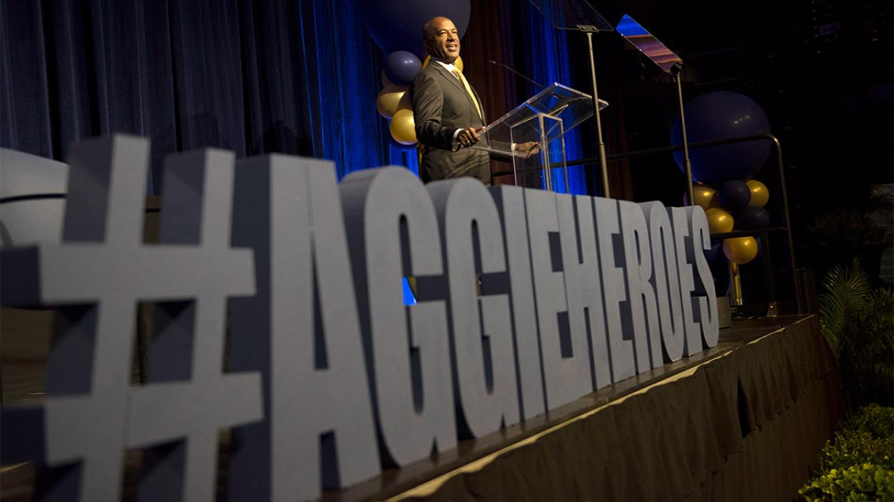 Chancellor Gary S. May speaks with a sign in front of him that reads #AggieHeroes.