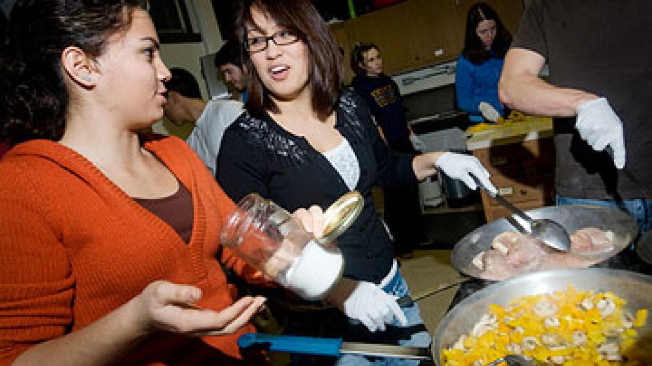 Photo: two women cooking over a stove in a busy place
