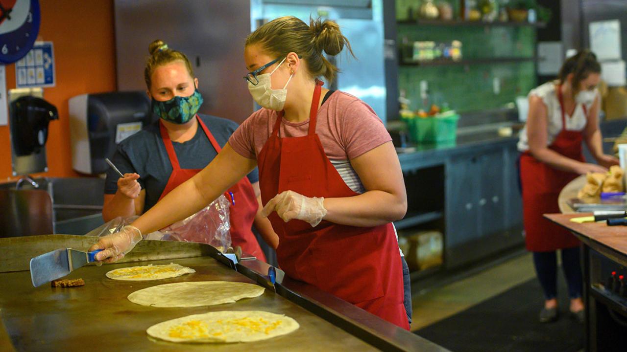 Two women cook burritos.