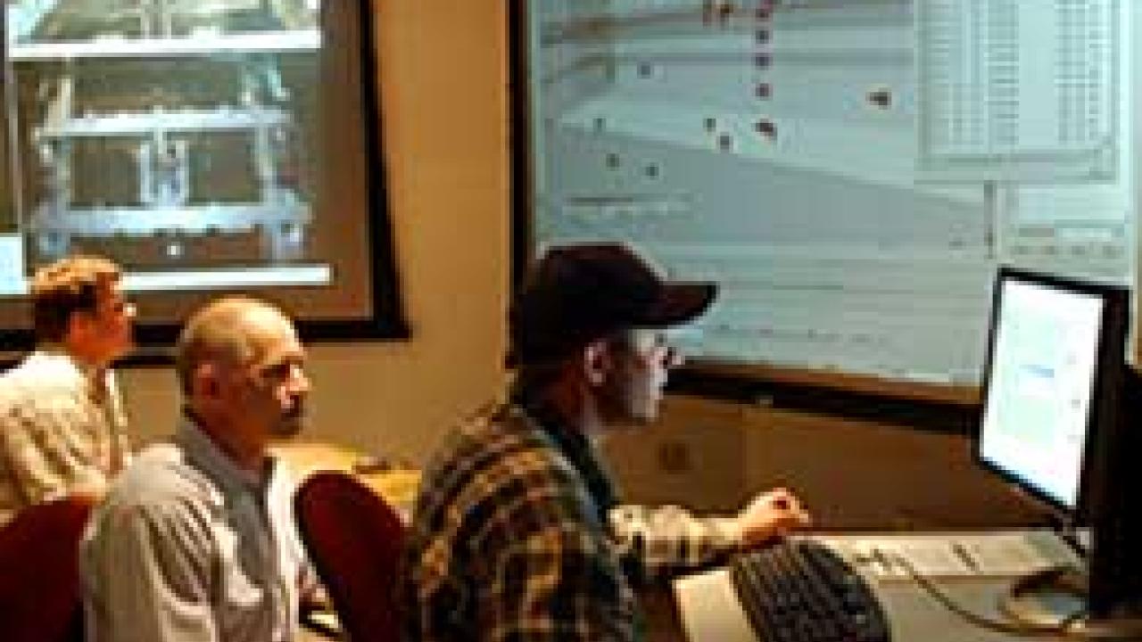 Photo: Three men in room looking at computers and screen