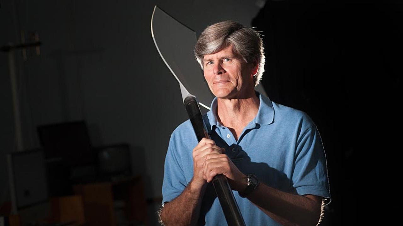 Man in light blue polo shirt holds oar.