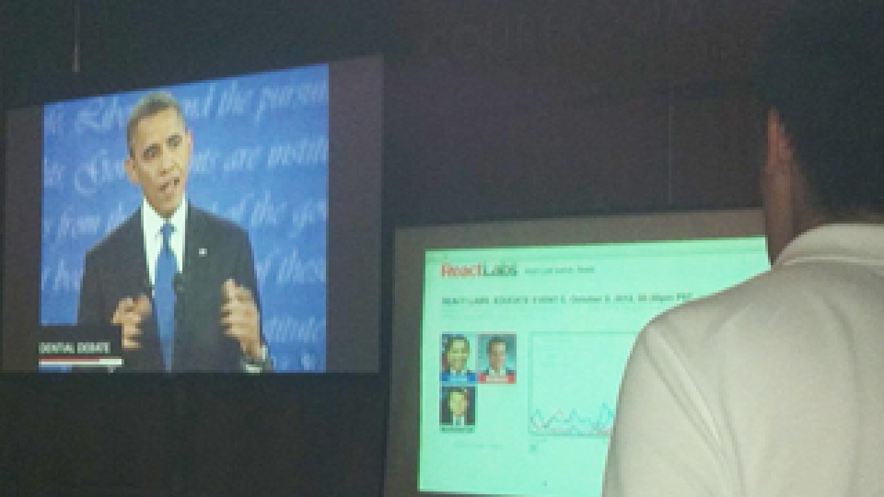Obama on video screen next to a monitor showing new app being watched by a man with his back to the camera