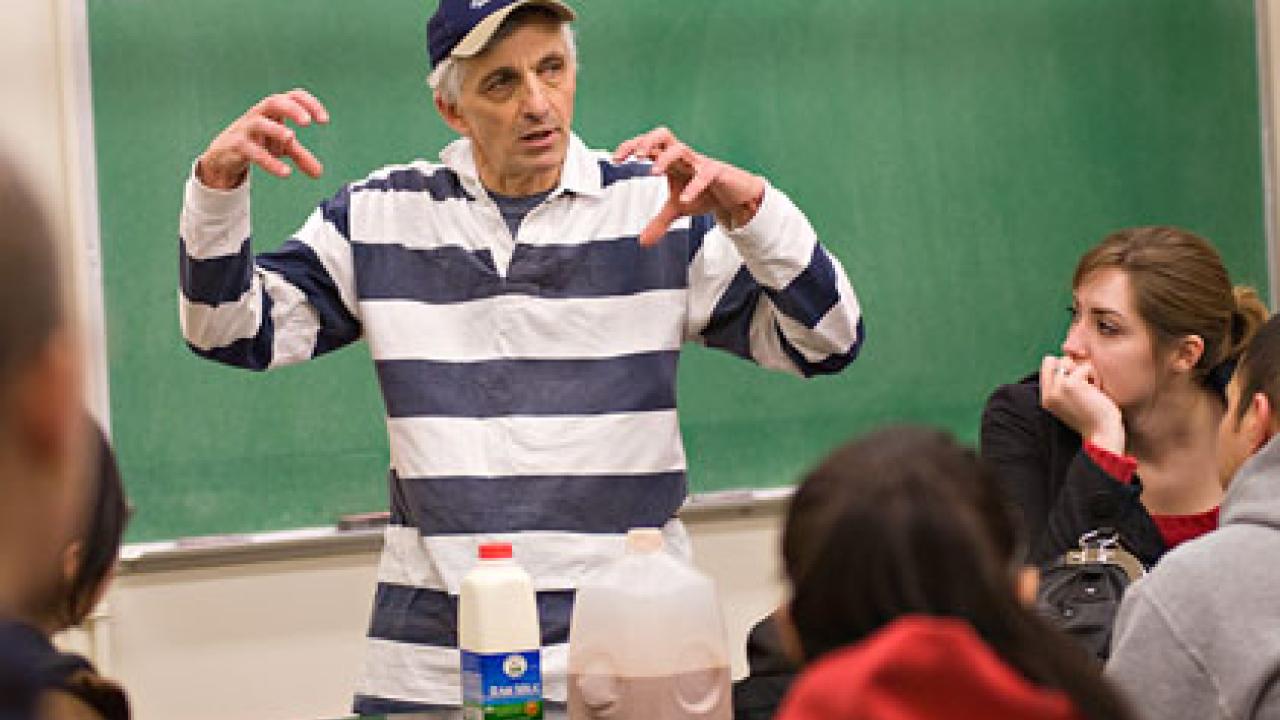 Photo: Ed DePeters gesturing in front of a blackboard with students listening. Bottles of milk and chocolate milk are on the desk.