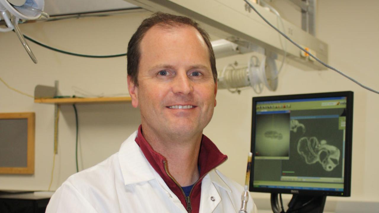 Doug Rowland in lab coat, standing next to imaging monitor