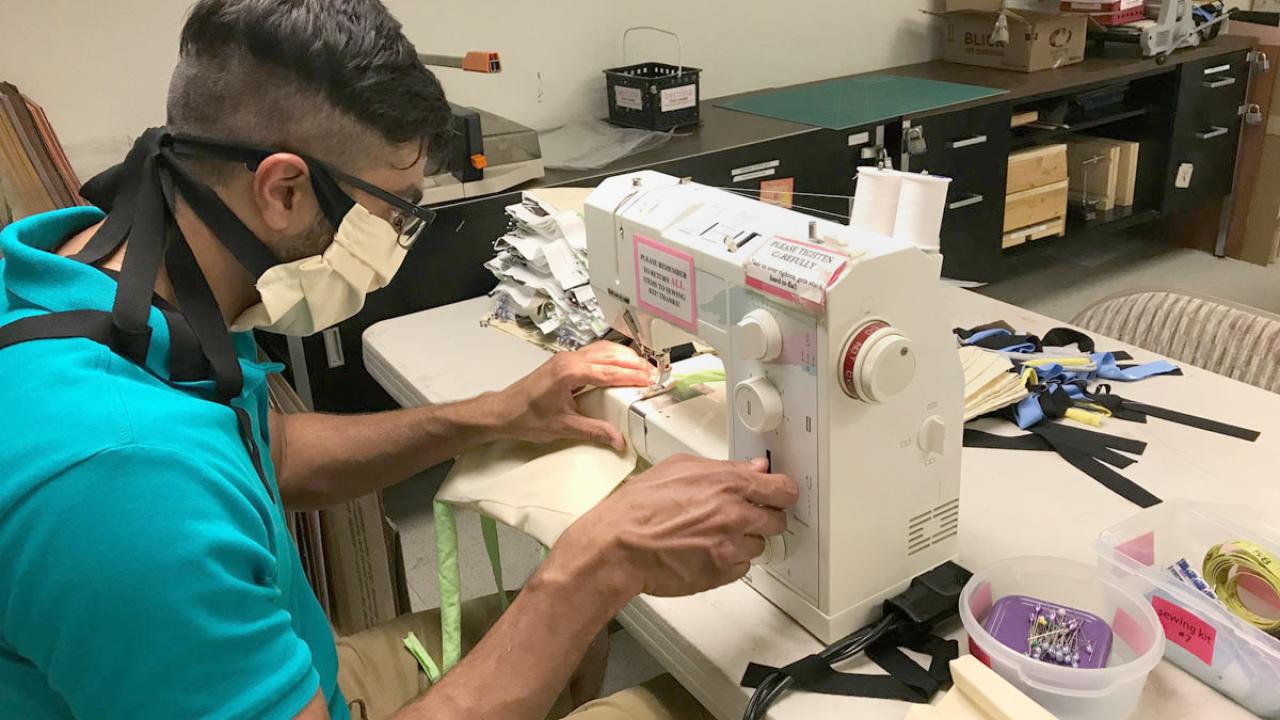 A man in face mask, works at sewing machine, making face masks.