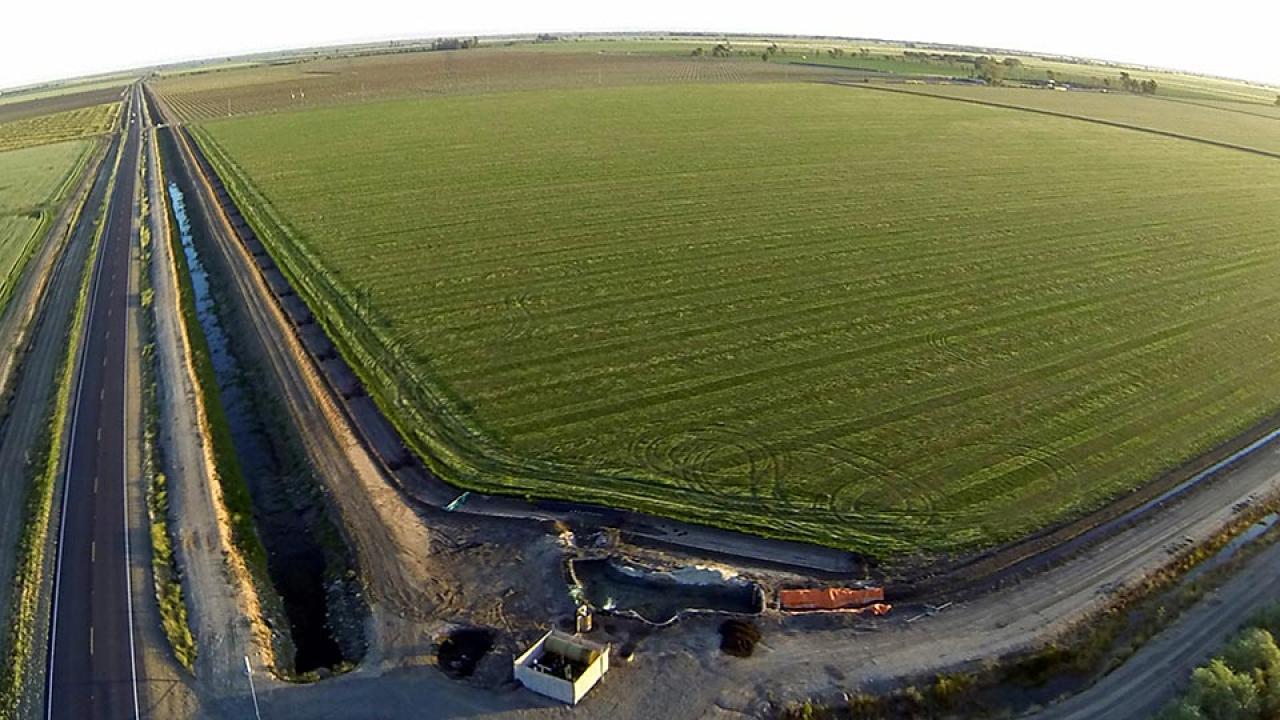 Green farm field bordered by irrigation canal, water pump and divided highway.