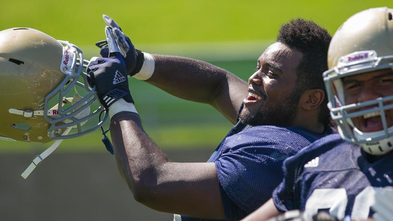 Two football players, one holding helmet and laughing, the other with helmet on