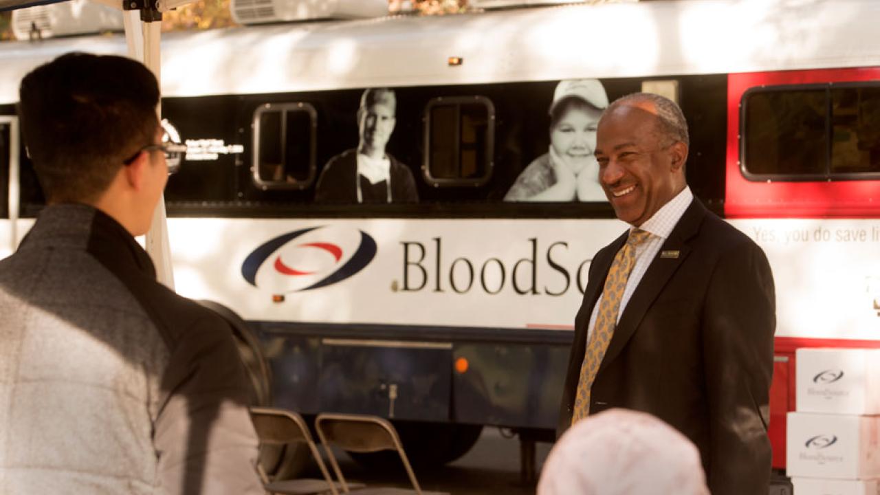 Chancellor Gary S. May chats with blood drive representatives, with bloodmobile in background, on the Quad.