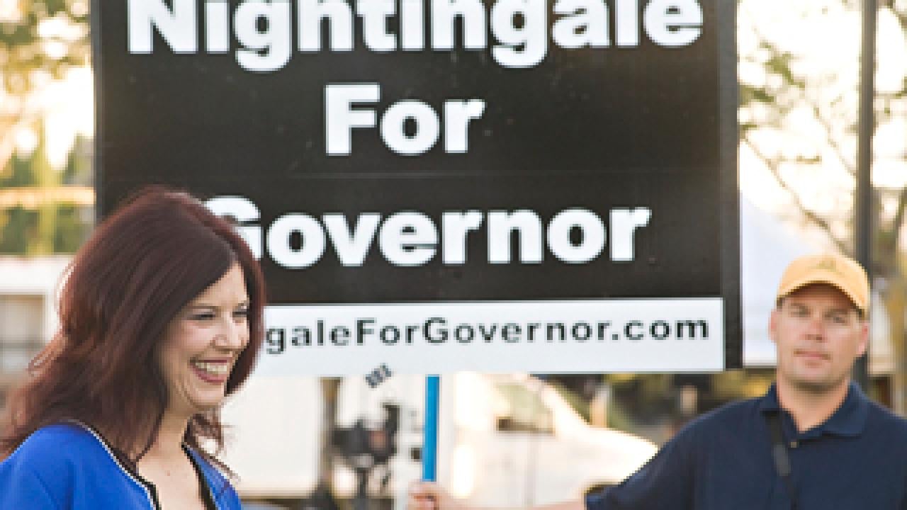 woman in front of sign "Nightingale for Governor" with man holding sign