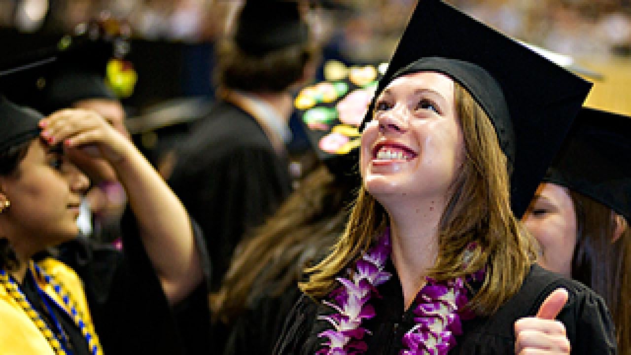 Female graduate in lei and mortarboard with thumb up