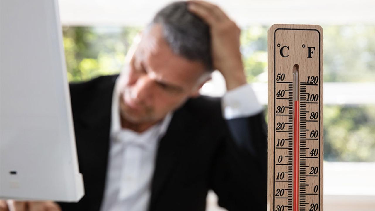 A thermometer in the foreground with a suited man at a computer in the background