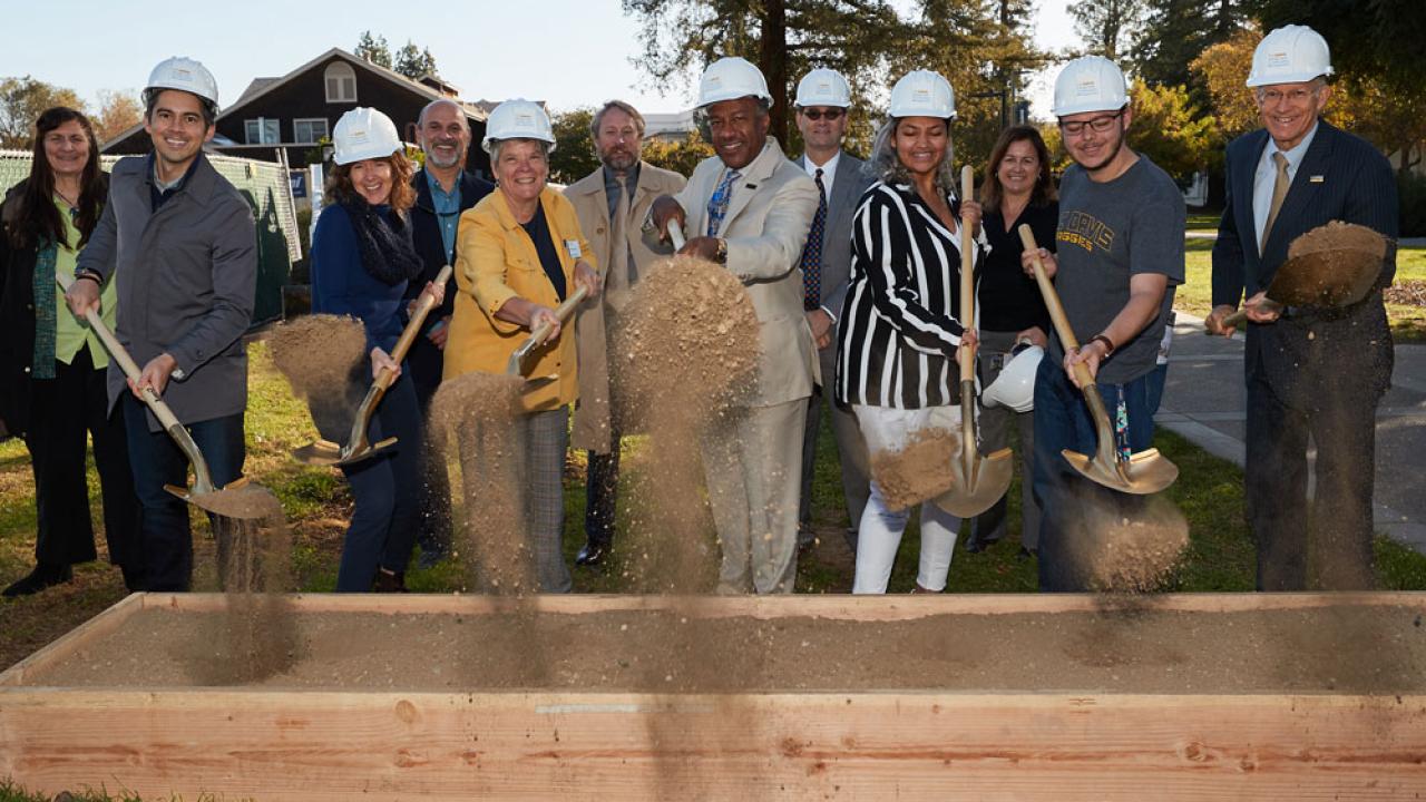 Dignitaries in hard hats, shoveling dirt into the air.