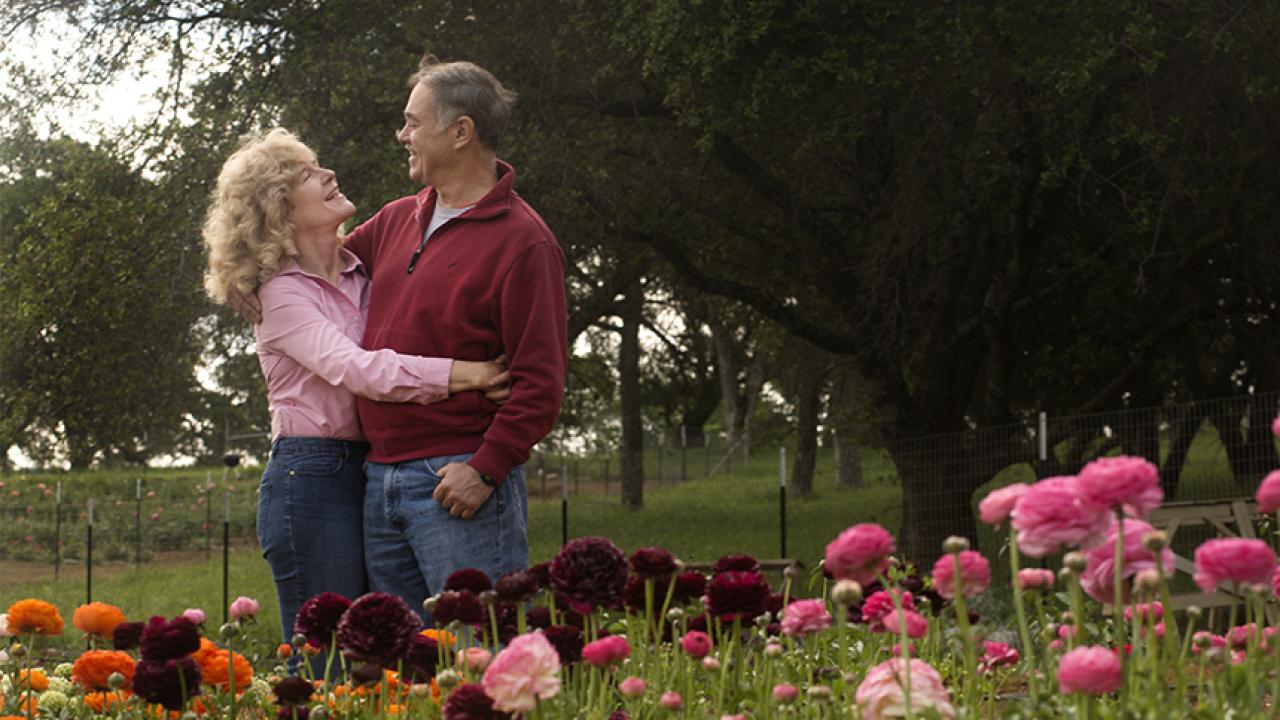 A couple embraces amid flowers and greenery