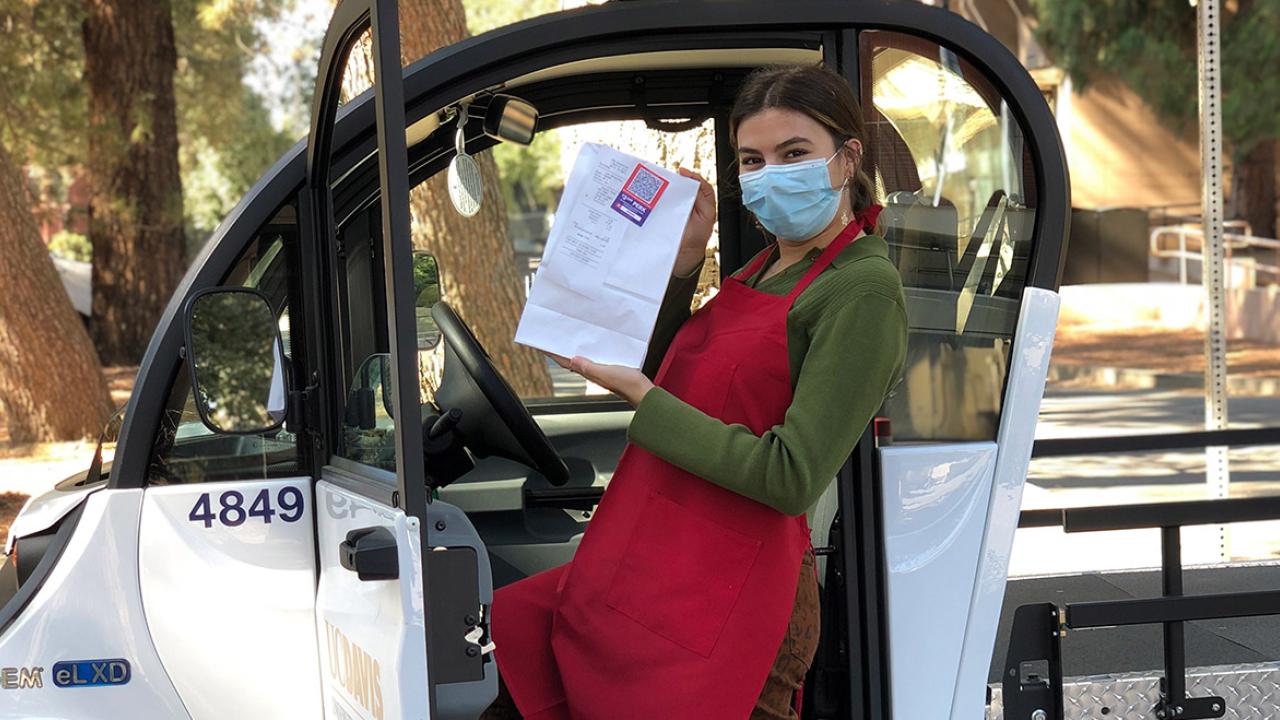 Woman wearing face covering holds food as she steps into electric cart.