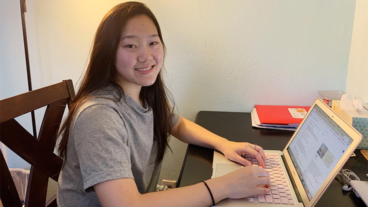 A female student sits at a desk with a laptop 